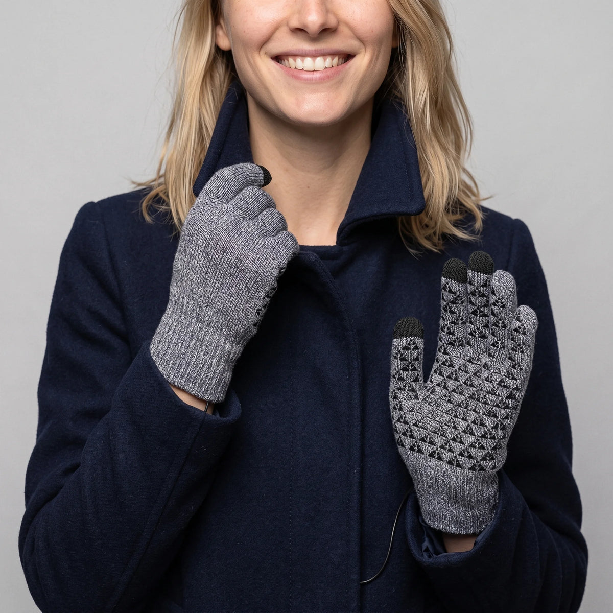 Gants chauffants tricotés gris chiné portés par une femme souriante en manteau marine