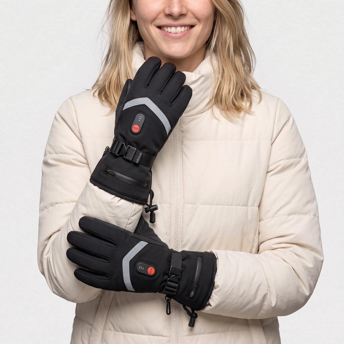 Gants chauffants à piles noirs portés par une femme souriante, une main au col de sa doudoune crème