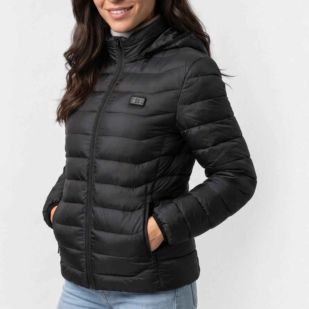 Veste chauffante noire à capuche portée par une femme souriante, mains dans les poches