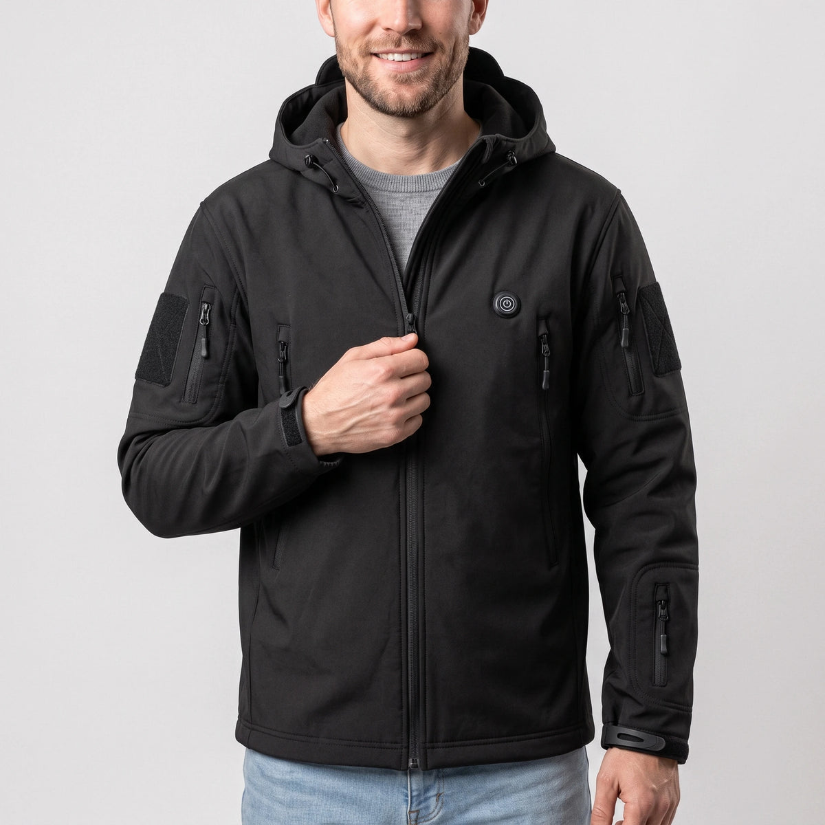 Veste softshell chauffante noire à capuche portée par un homme, une main sur la fermeture