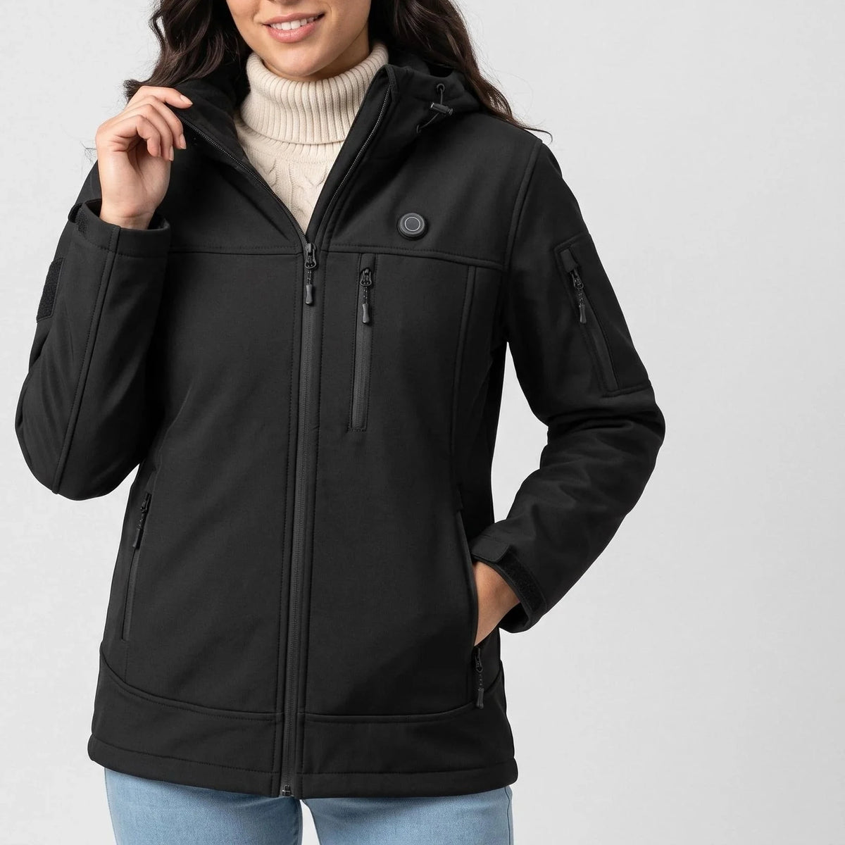 Veste chauffante noire à capuche portée par une femme souriante, une main au col