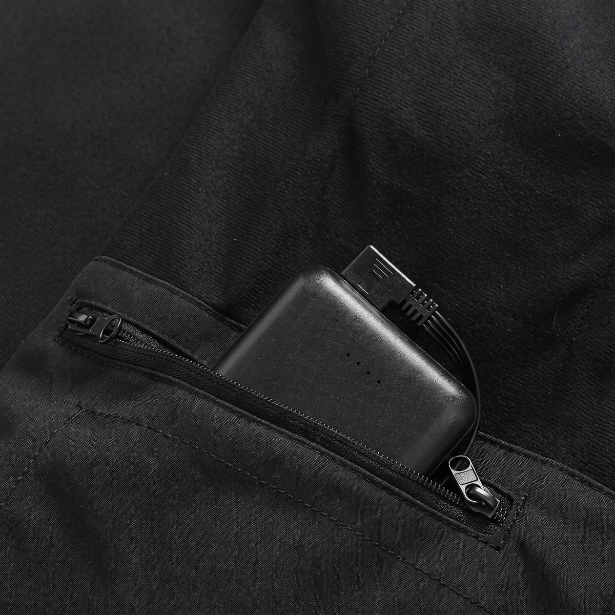 Poche intérieure zippée du gilet avec une batterie externe glissée dedans, batterie non incluse