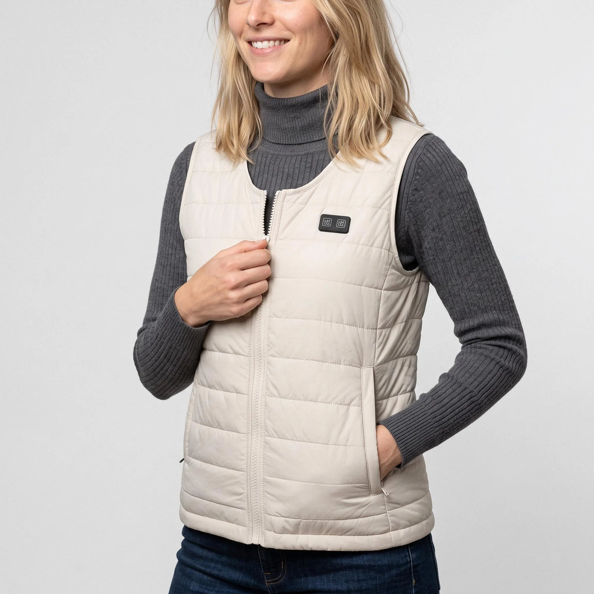 Gilet chauffant léger beige clair porté par une femme, une main sur la fermeture