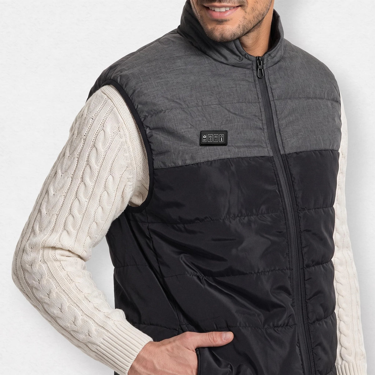 Gilet chauffant matelassé bicolore gris anthracite et noir porté par un homme souriant, pull torsadé écru