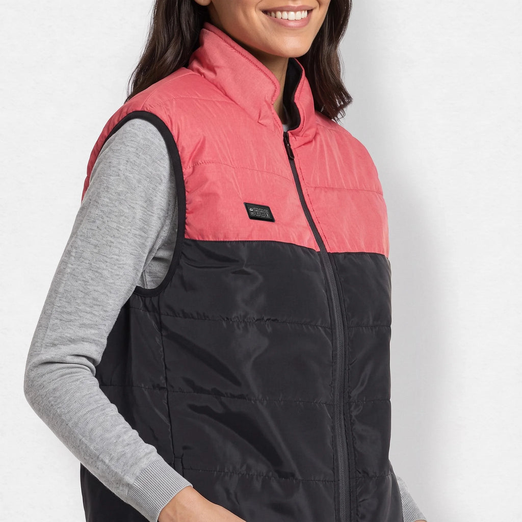 Gilet chauffant matelassé bicolore rose et noir porté par une femme souriante, haut gris chiné