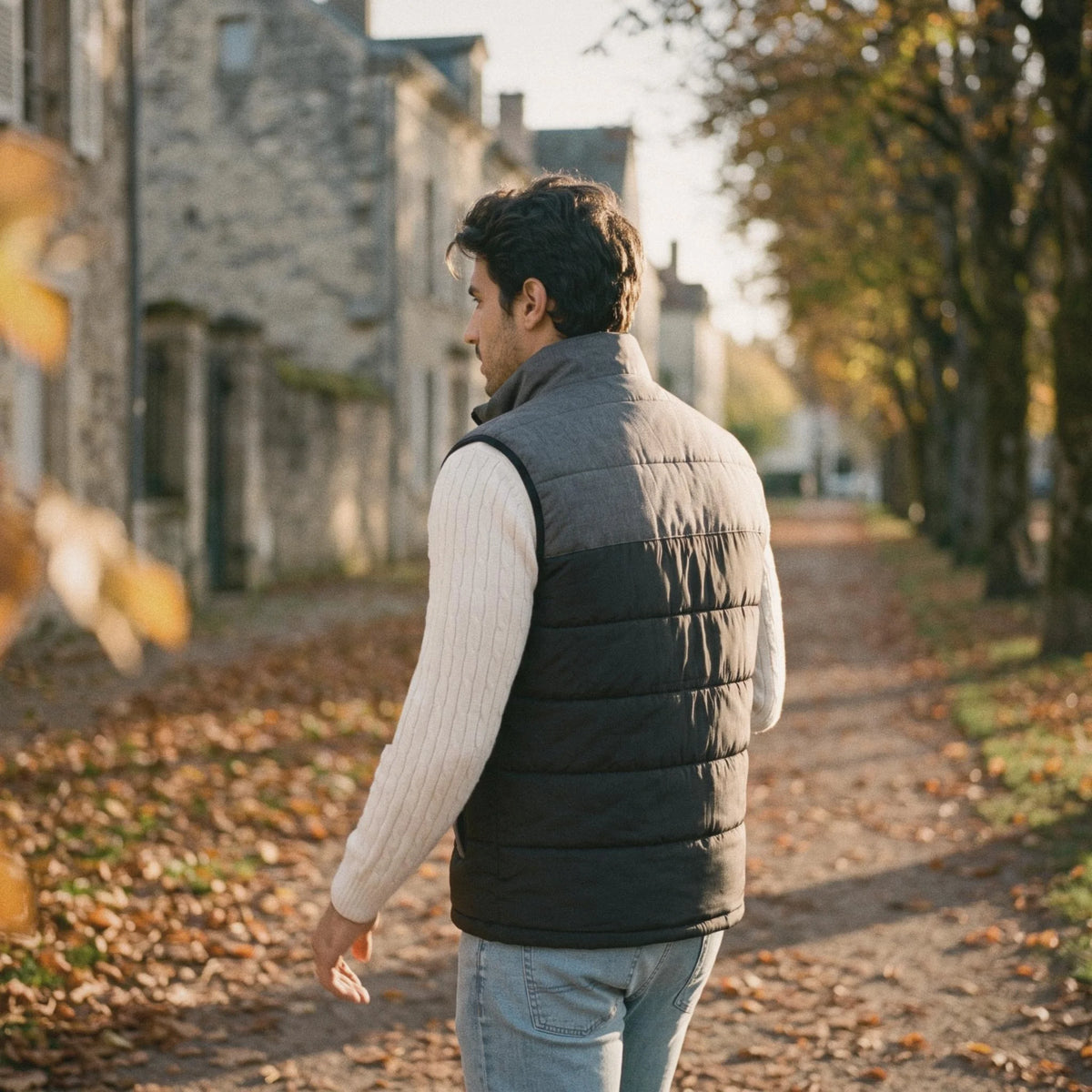 Homme de dos en gilet chauffant gris anthracite et noir, marchant dans une allée de parc en automne