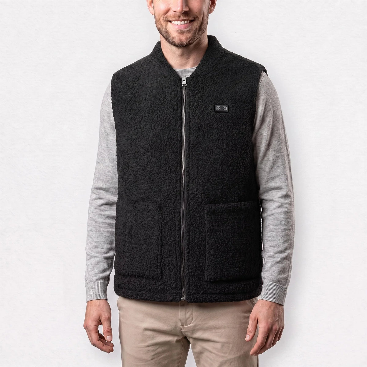 Gilet chauffant en polaire sherpa noir porté par un homme souriant, pull gris clair et chino sable