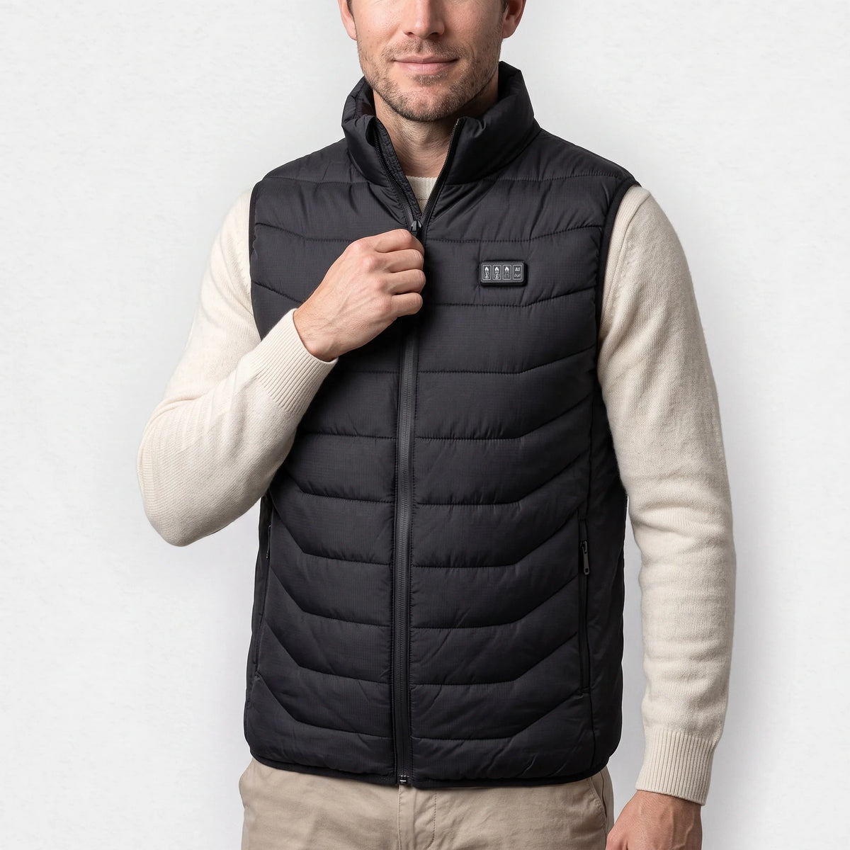 Gilet chauffant noir porté par un homme souriant, pull écru, boîtier à 4 boutons sur la poitrine