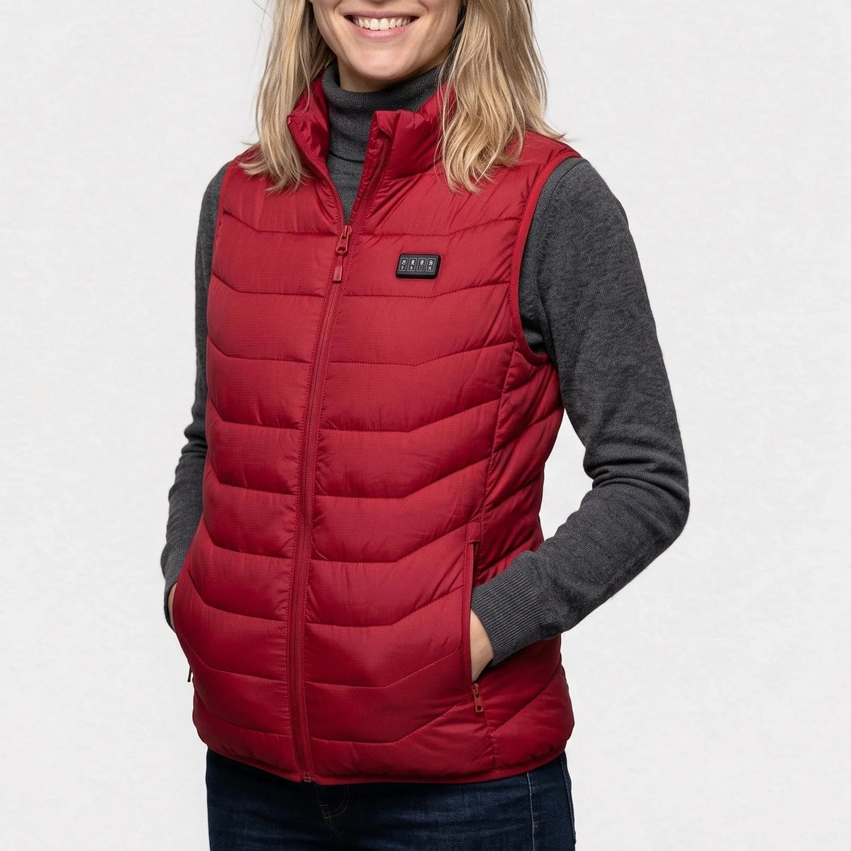 Gilet chauffant rouge porté par une femme souriante, les mains dans les poches