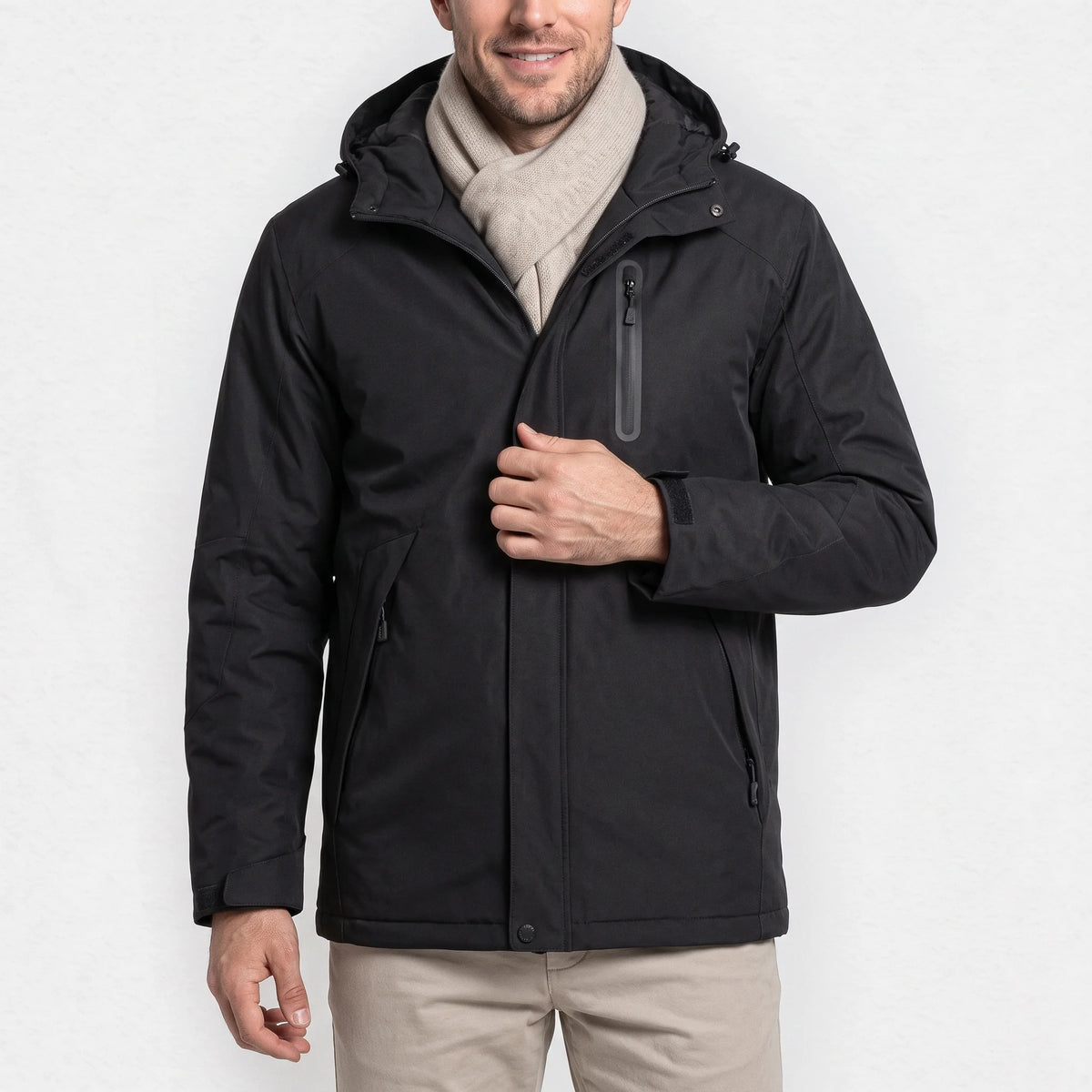 Veste chauffante homme noire à capuche portée par un homme souriant qui tient sa fermeture