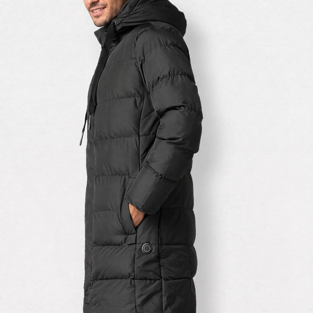 Parka chauffante longue noire portée de profil, une main dans la poche, bouton rond à la hanche