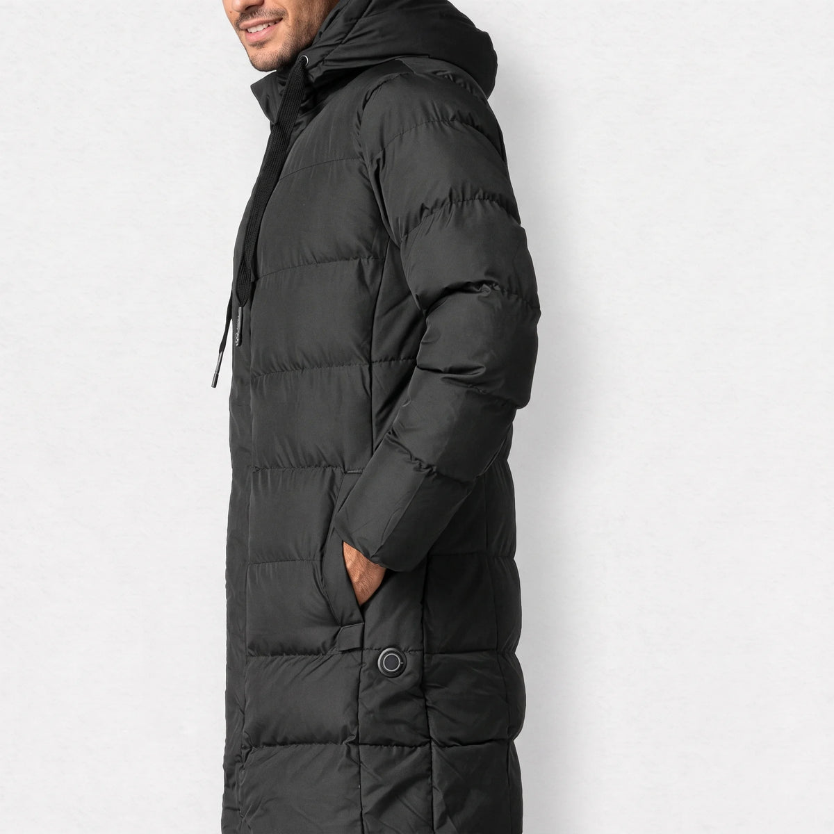 Parka chauffante longue noire portée de profil, une main dans la poche, bouton rond à la hanche