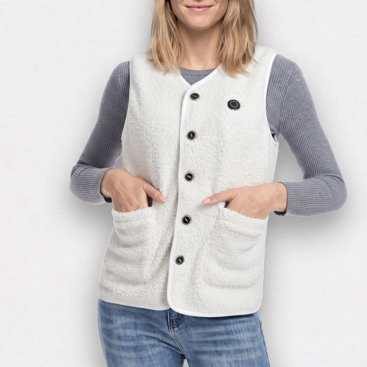 Gilet chauffant sherpa blanc porté par une femme souriante, les mains dans les poches