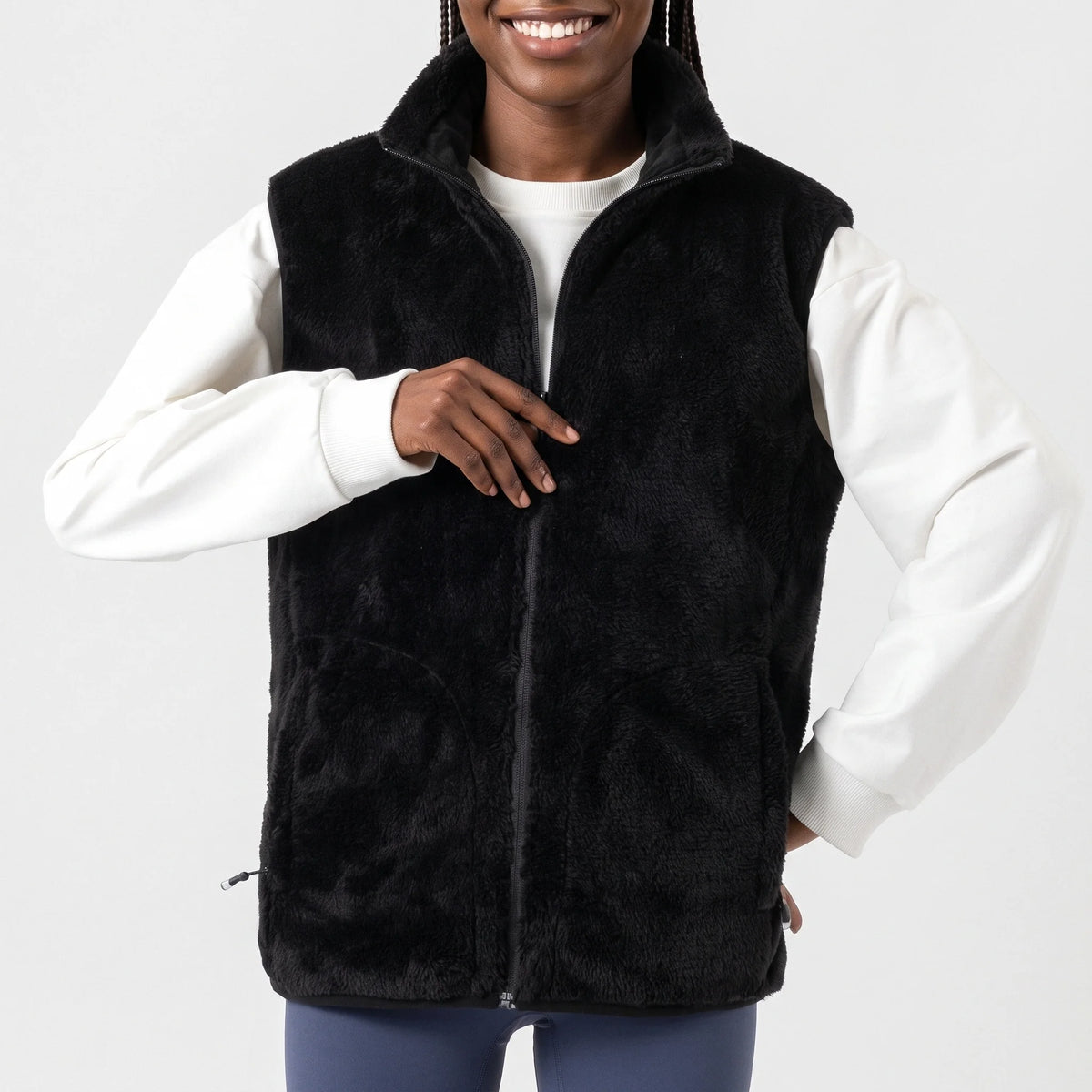 Gilet chauffant en peluche noir porté par une femme souriante, une main sur la fermeture