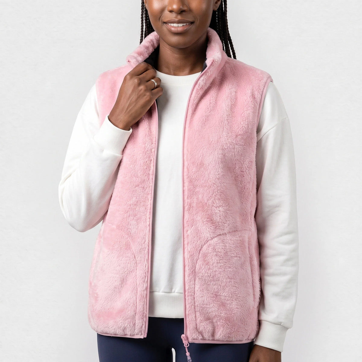 Gilet chauffant en peluche rose clair porté ouvert par une femme souriante qui tient son col
