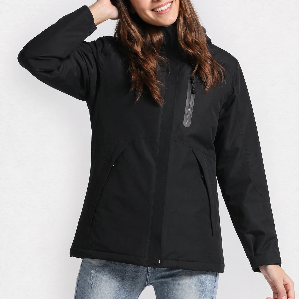 Veste chauffante femme noire à capuche portée par une femme souriante, une main dans les cheveux