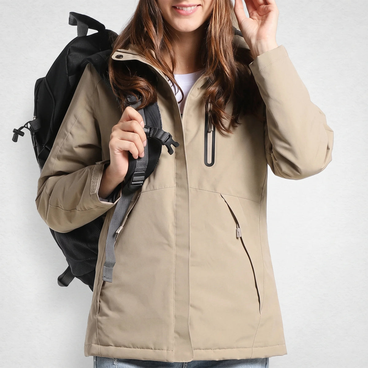 Veste chauffante femme sable à capuche portée par une femme souriante avec un sac à dos