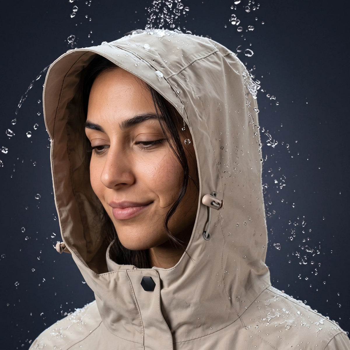 Femme sous les gouttes d'eau, capuche relevée : l'eau perle sur le tissu déperlant de la veste sable