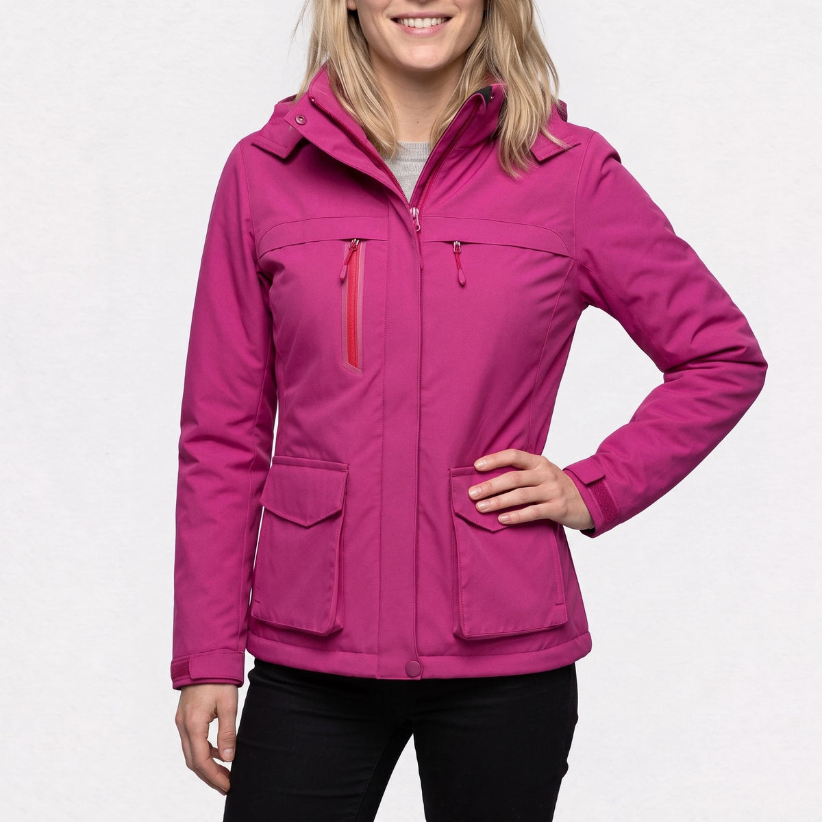 Veste de ski chauffante fuchsia portée par une femme souriante, une main sur la hanche