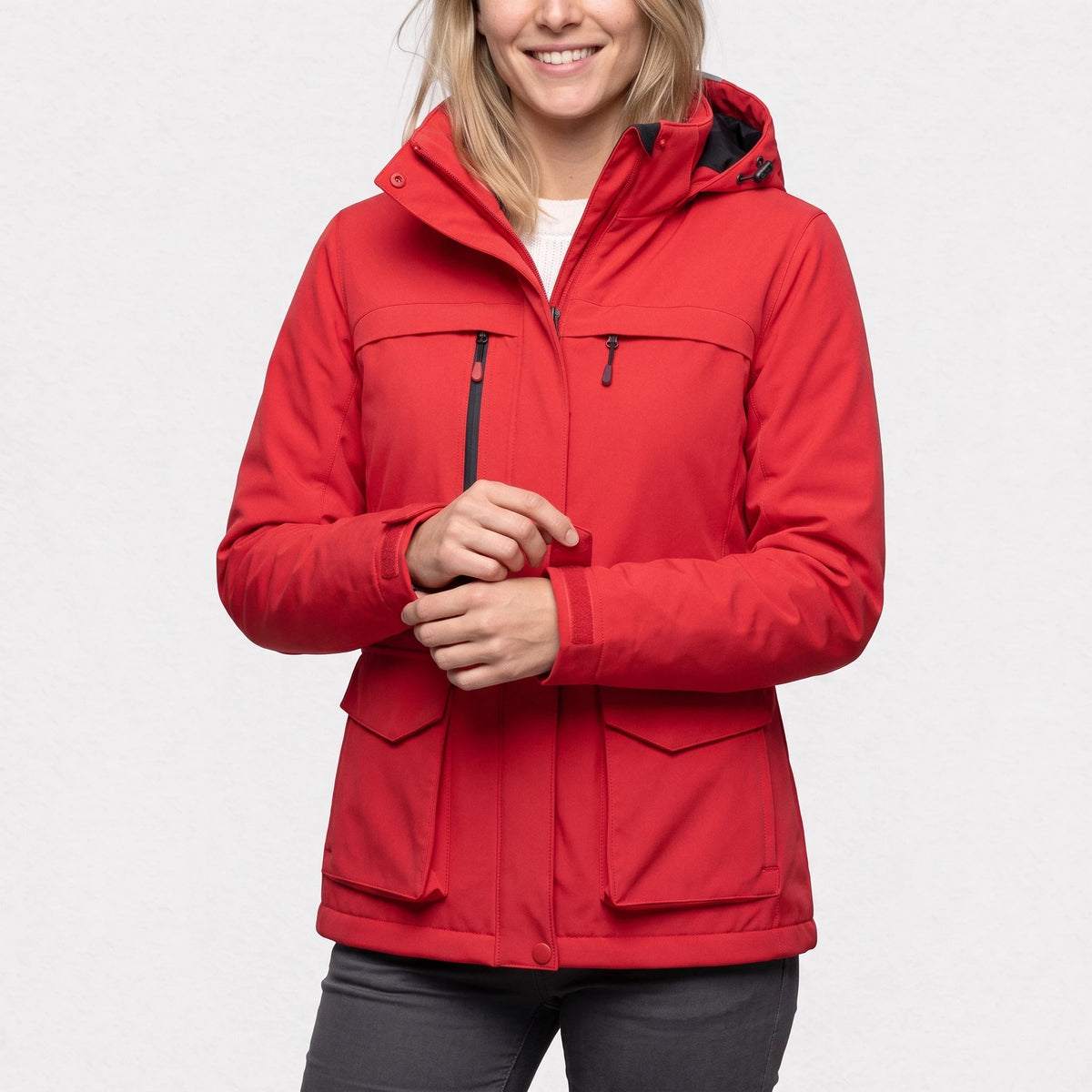 Veste de ski chauffante rouge portée par une femme souriante qui ajuste son poignet